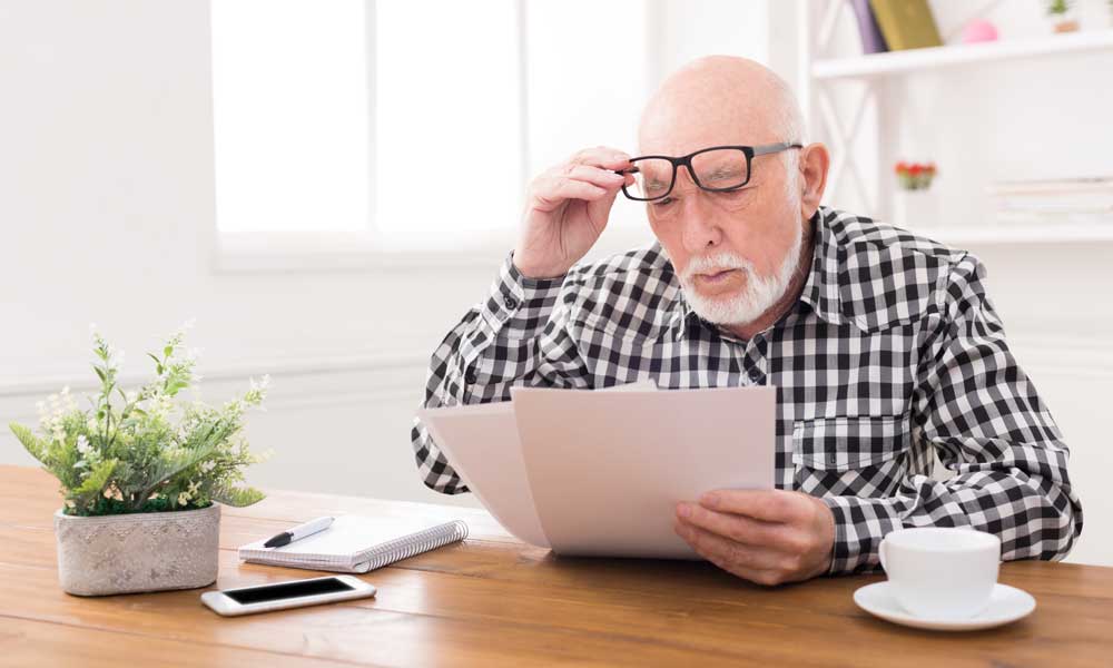 man removing his glasses to see the paper better